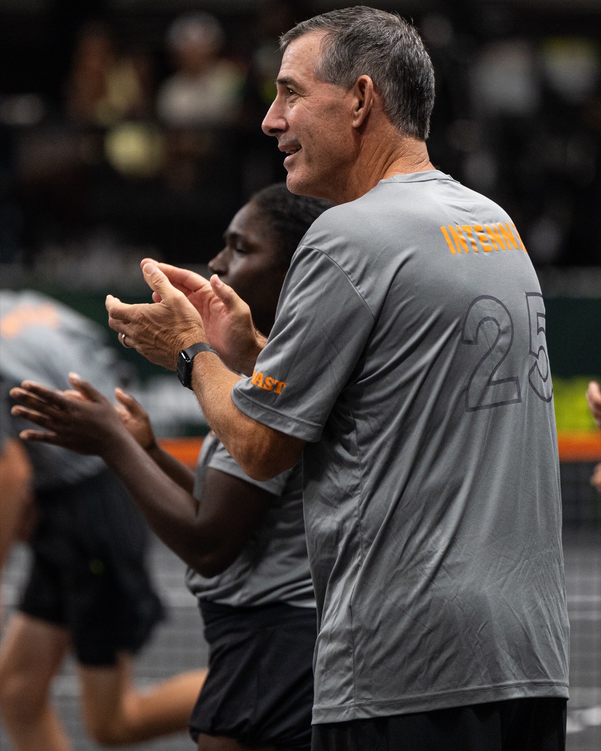 A coach in a grey Challenge shirt applauding courtside alongside a player.